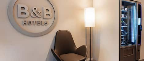 A B&B hotel reception area with a modern chair, a wall-mounted sign, and a vending machine.