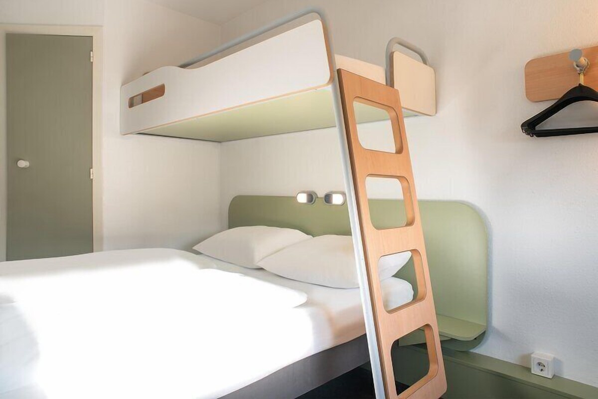 Un lit superposé avec une échelle en bois, une table de chevet et un luminaire fixé au mur.