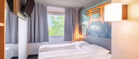 A hotel room with a bed, a TV mounted on the wall, a window with curtains, and a mural of a bridge.