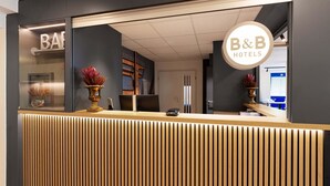 A reception desk with a modern design, featuring vertical wooden slats and two decorative vases with red flowers. -  B&B HOTEL Essen-Nord (Essen)