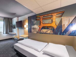 Hotelkamer met een bed, bureau, stoel, televisie en een grote muurschildering.