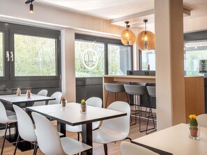 Un espace de restauration moderne, doté de tables et de chaises, de grandes fenêtres et de luminaires suspendus.