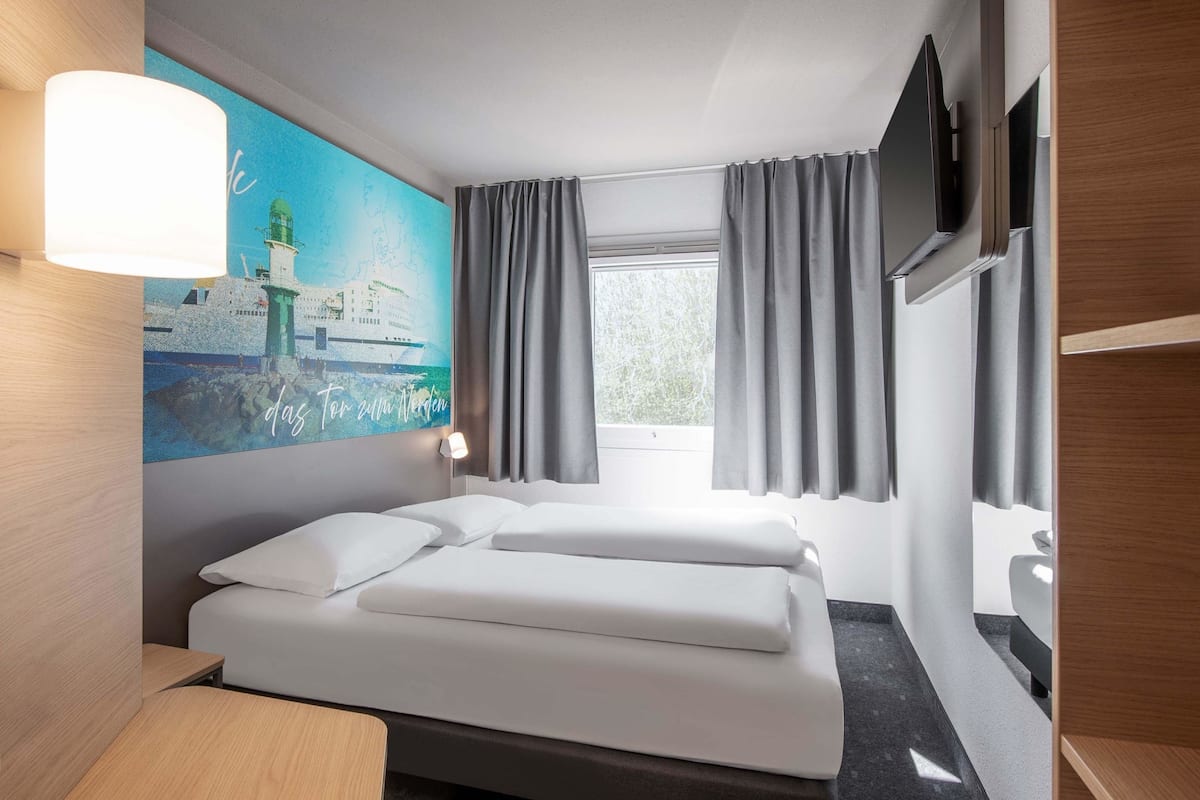 Ein Hotelzimmer mit einem Bett, einem Leuchtturm-Gemälde, einem Fernseher und einem Fenster mit Vorhängen.