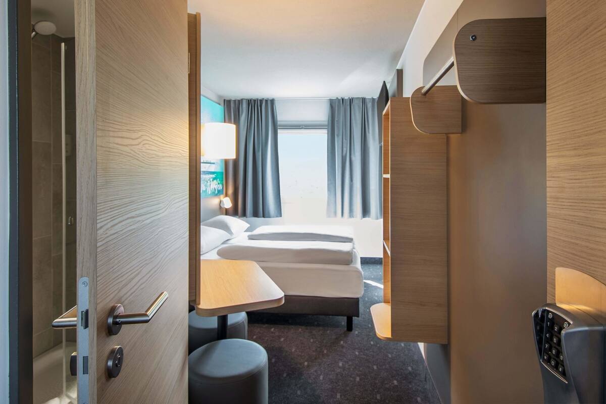 Ein Hotelzimmer mit Bett, Nachttisch, Stuhl und Blick ins Freie.