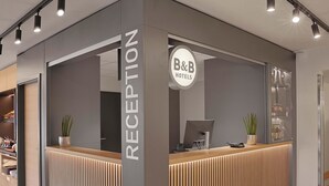A reception area with a modern design, featuring a reception desk, a computer, and a sign that reads "B&B Hotels." - B&B HOTEL Berlin Genshagen-Nord (Ludwigsfelde)
