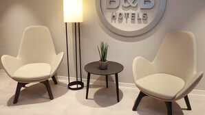 Two modern armchairs, a floor lamp, and a small table with a plant, all against a wall with a 'B&B HOTELS' sign. - B&B HOTEL Berlin Genshagen-Nord (Ludwigsfelde)