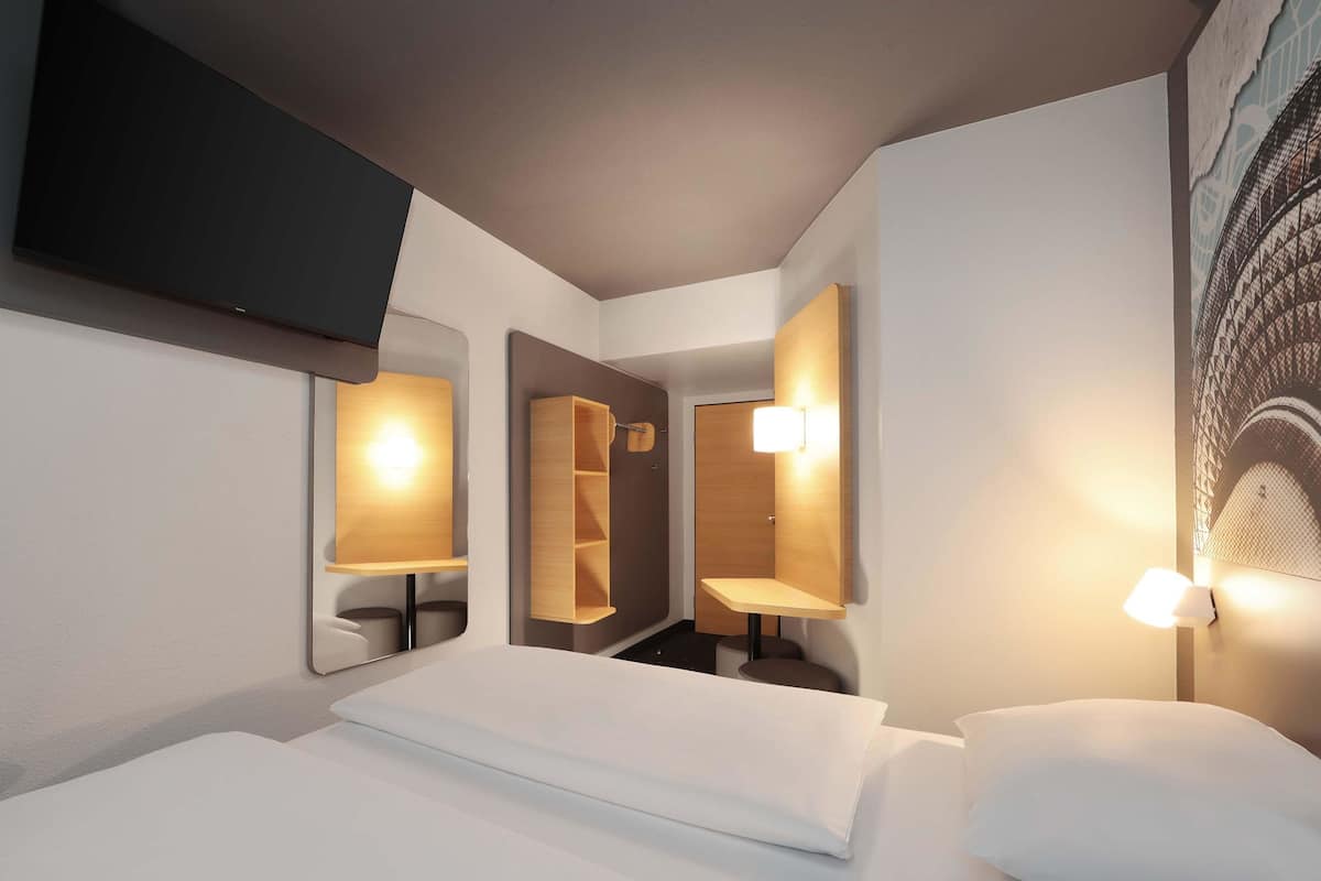 A modern hotel room with a neatly made bed, built-in shelves, and wall-mounted lamps.