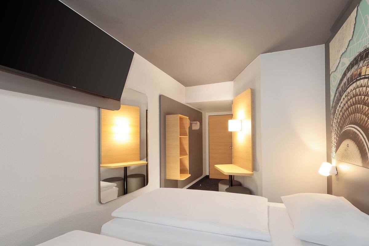 A modern hotel room with a bed, a TV mounted on the wall, and a painting of the Eiffel Tower.
