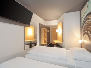 Une chambre d’hôtel moderne, équipée d’un lit, d’un téléviseur fixé au mur et d’un tableau représentant la Tour Eiffel.