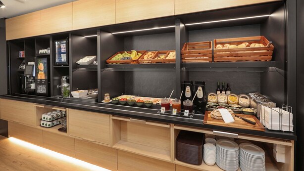 A buffet setup with various food items, beverages, and condiments. - B&B HOTEL Berlin Genshagen-Nord (Ludwigsfelde)