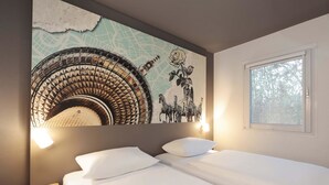A hotel room with a bed, a small bedside table, a wall-mounted lamp, and a window with a view of trees. - B&B HOTEL Berlin Genshagen-Nord (Ludwigsfelde)