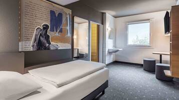 Ein modernes Hotelzimmer mit einem Bett, einem großen Spiegel, einem Fenster und einem kleinen Tisch.