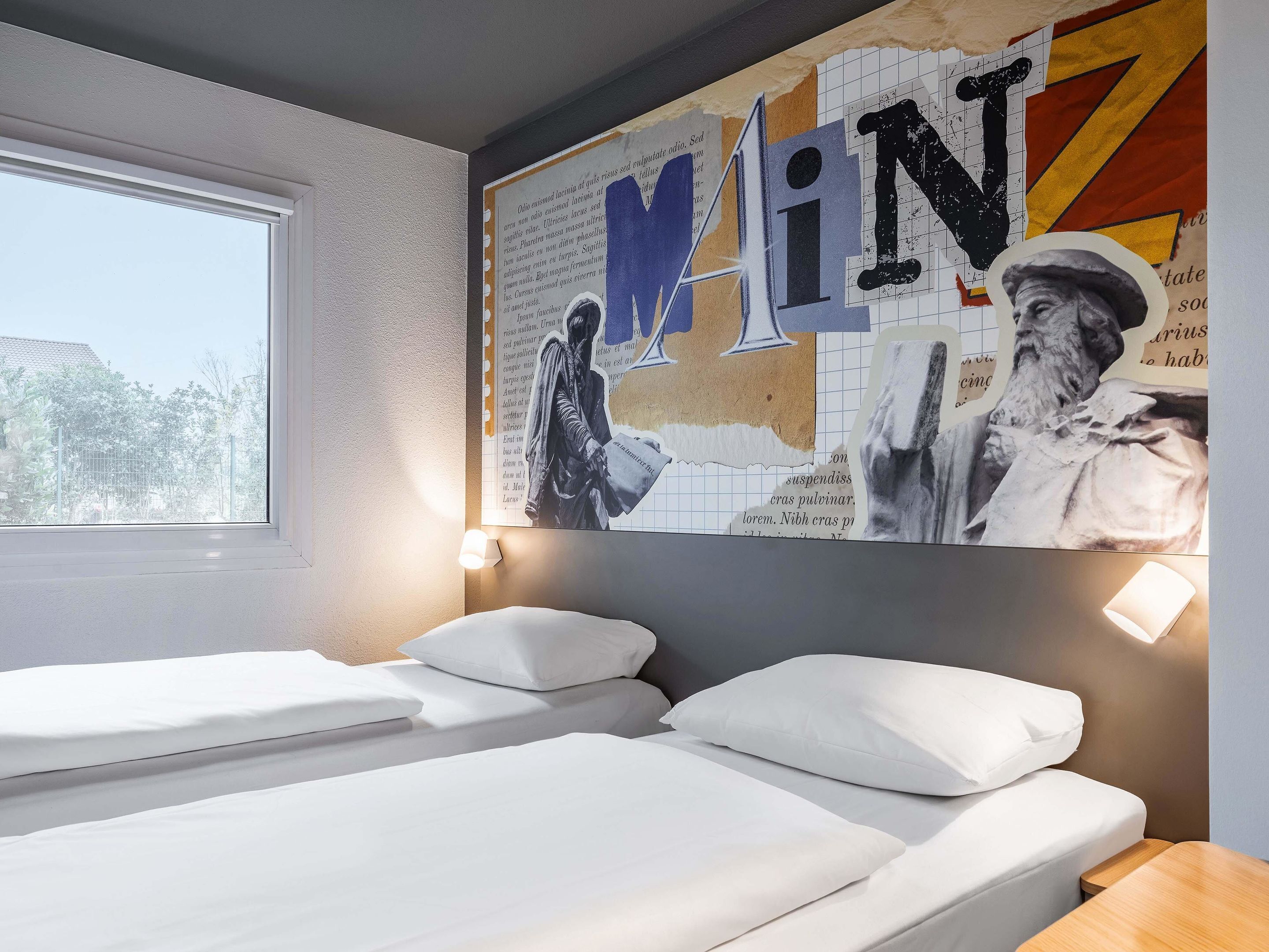 Hotellihuone, jossa on kaksi sänkyä, suuri seinämaalaus ja ikkuna, josta avautuu näkymä puihin.