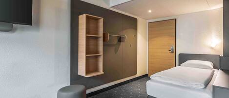 Una habitación de hotel moderna con cama, armario, estante empotrado, reposapiés redondo y televisor de pantalla plana.