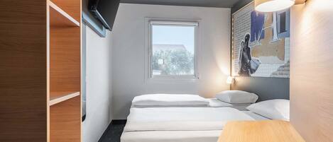 Habitación de hotel con cama, mesitas de noche, televisor montado en la pared y ventana con vistas al exterior.
