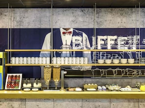 A buffet counter with a large sign, multiple serving stations, and a variety of food and drink options. - ibis budget Krefeld Messe Duesseldorf (Krefeld)
