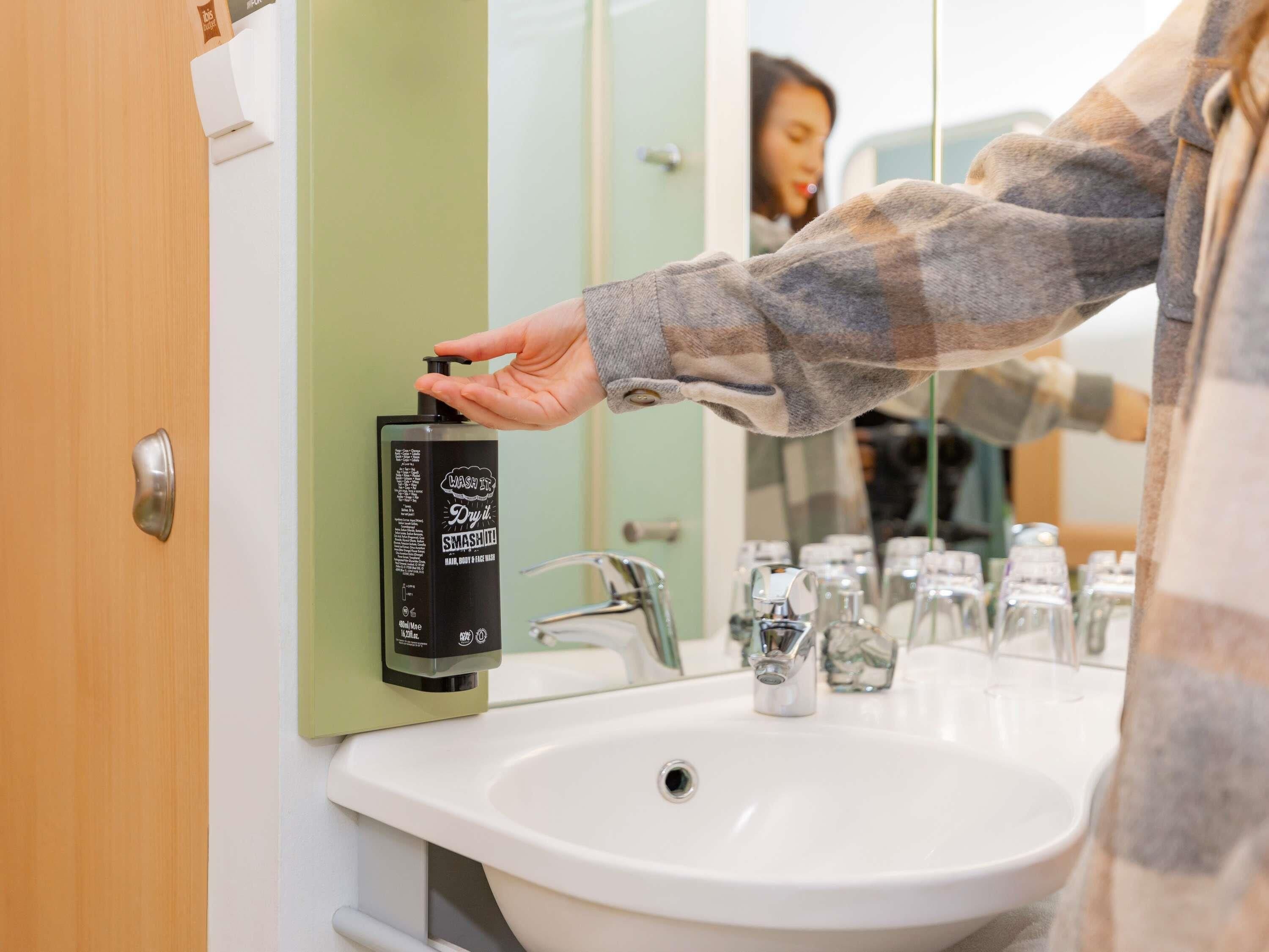 A person using a black hand dryer mounted on a wall next to a white sink in a bathroom.