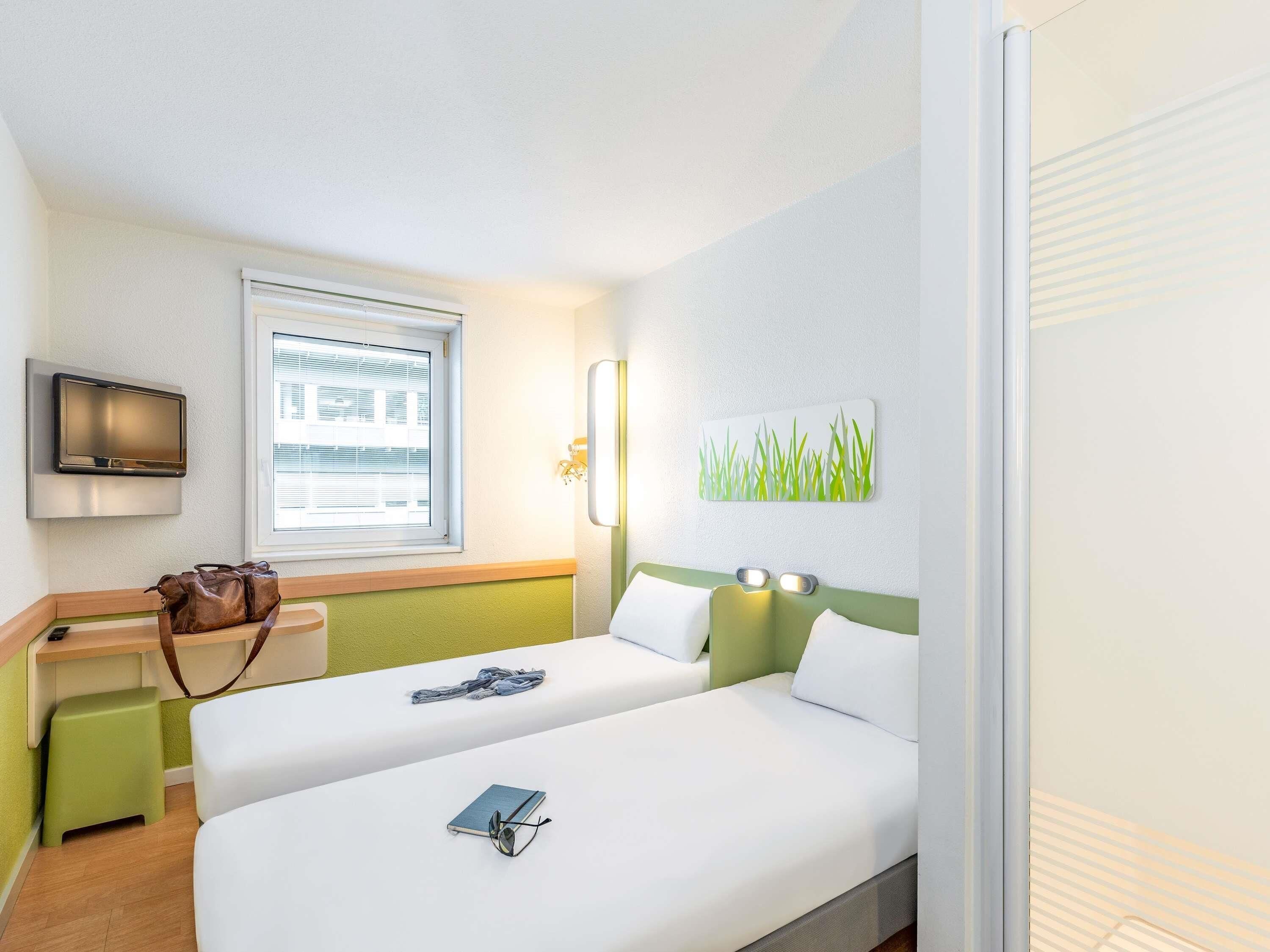A hotel room with two beds, a desk, a television, and a window with blinds.