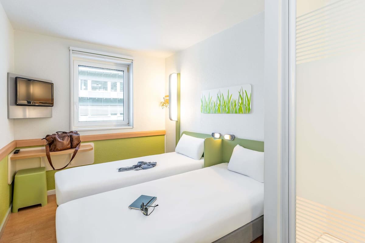 A hotel room with two beds, a desk, a television, and a window with blinds.