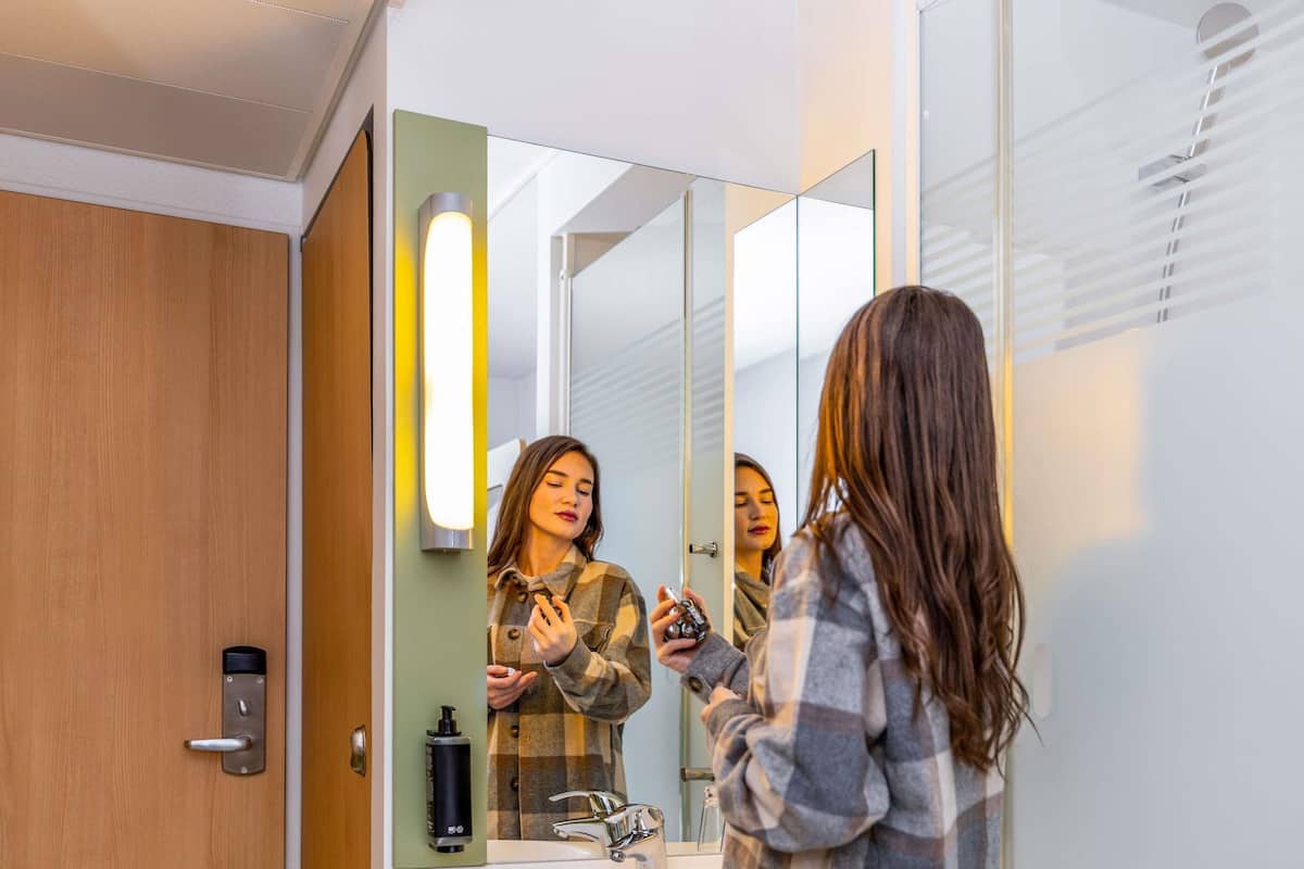 A modern bathroom with a wooden door, a mirror, a sink, and a hand sanitizer dispenser.