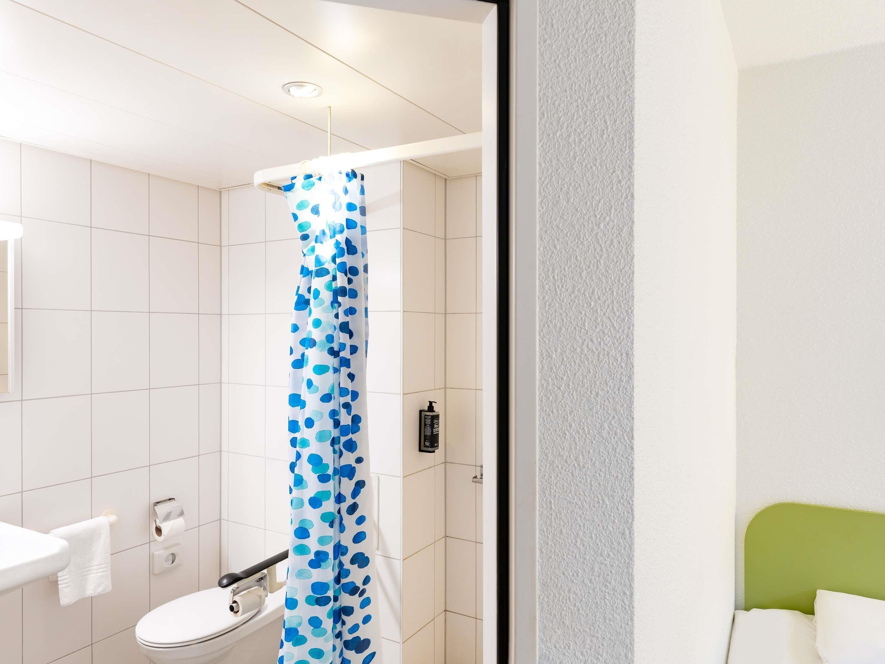 Une salle de bain avec des toilettes blanches, un rideau de douche à pois bleus, un lavabo blanc et une tête de lit verte.