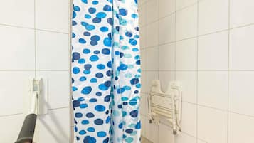 Un baño con cortina de ducha a lunares azules y verde azulado, pared de azulejos blancos y radiador blanco.