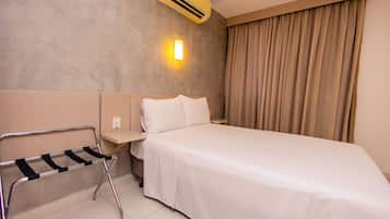 Habitación de hotel con cama, mesita de noche, aire acondicionado instalado en la pared y un perchero para toallas.