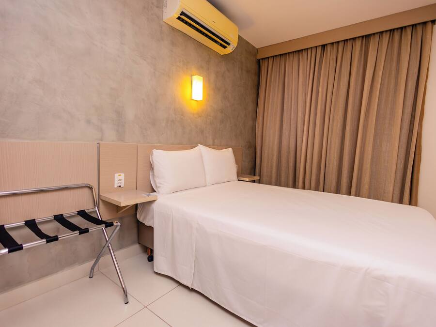 Habitación de hotel con cama, mesita de noche, aire acondicionado instalado en la pared y un perchero para toallas.