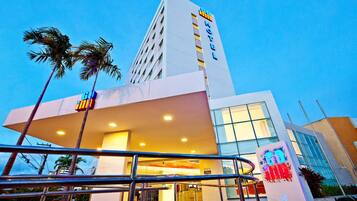Hotel entrance with a flat roof and large windows, surrounded by palm trees.