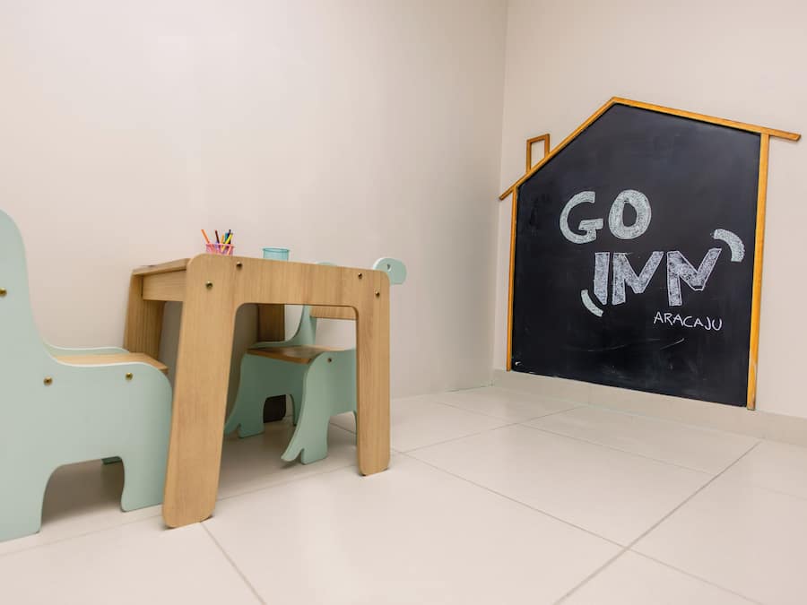 Una habitación con una mesa de madera y dos sillas a juego, una pizarra con la inscripción 'GO IN' y un pequeño modelo de casa de madera.