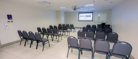 A conference room with rows of chairs, a projector screen, and a whiteboard.