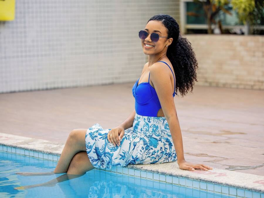 Una persona sentada junto a una piscina, con un muro de azulejos al fondo.