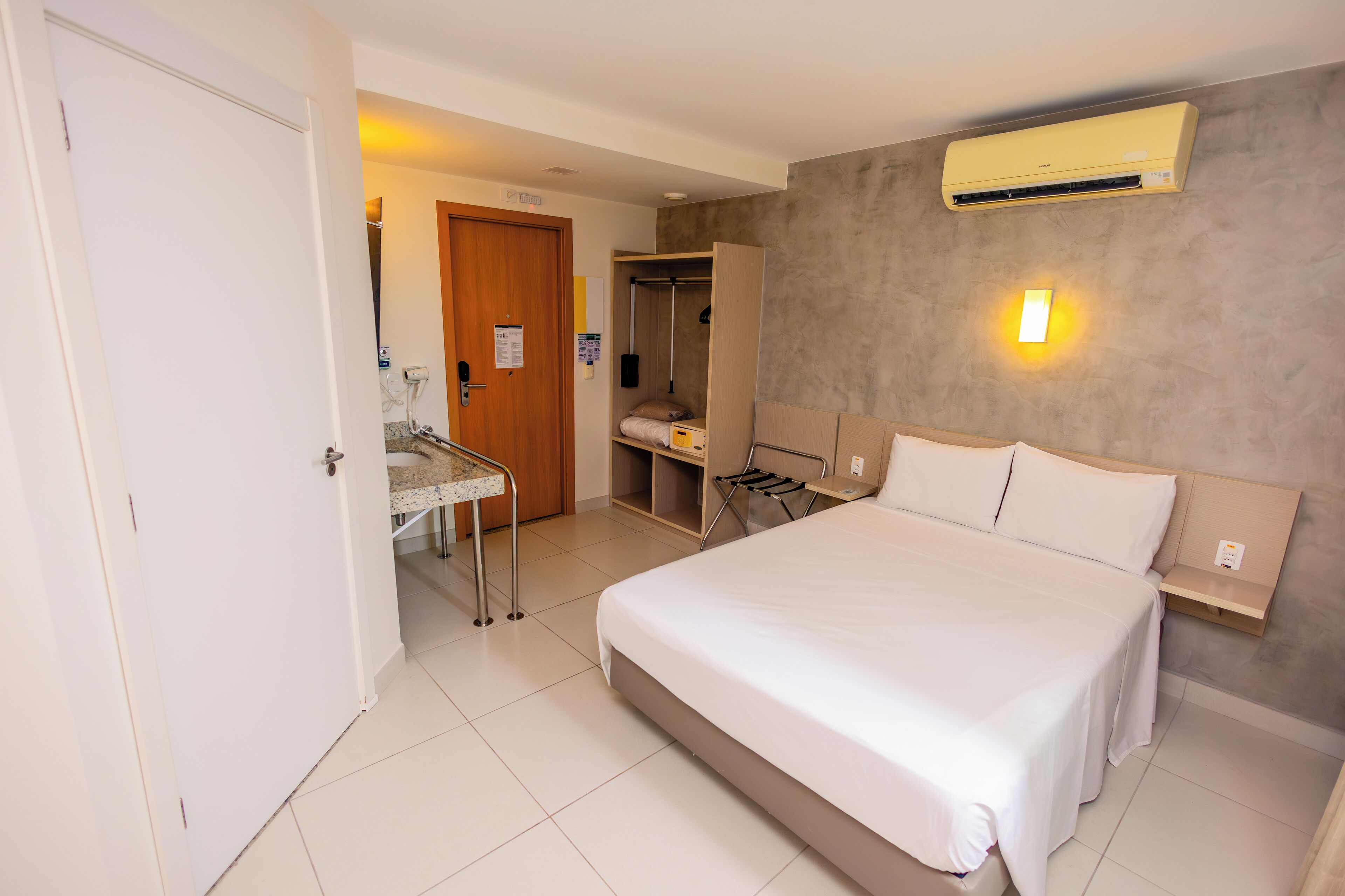 Habitación de hotel con una cama grande, un armario, un escritorio con silla y un equipo de aire acondicionado en la pared.