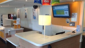 A reception area with a counter, a computer monitor displaying a booking interface, and a wall-mounted TV. - ibis budget Orgeval (Orgeval)
