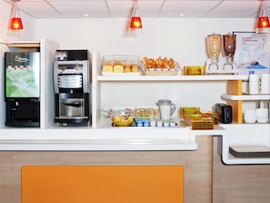 A hotel reception area with a coffee machine, a refrigerator, a fruit bowl, and a buffet with bread and pastries. - ibis budget Orgeval (Orgeval)