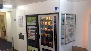 A vending machine with a variety of snacks and drinks, a fire extinguisher, and a small plant. - ibis budget Orgeval (Orgeval)