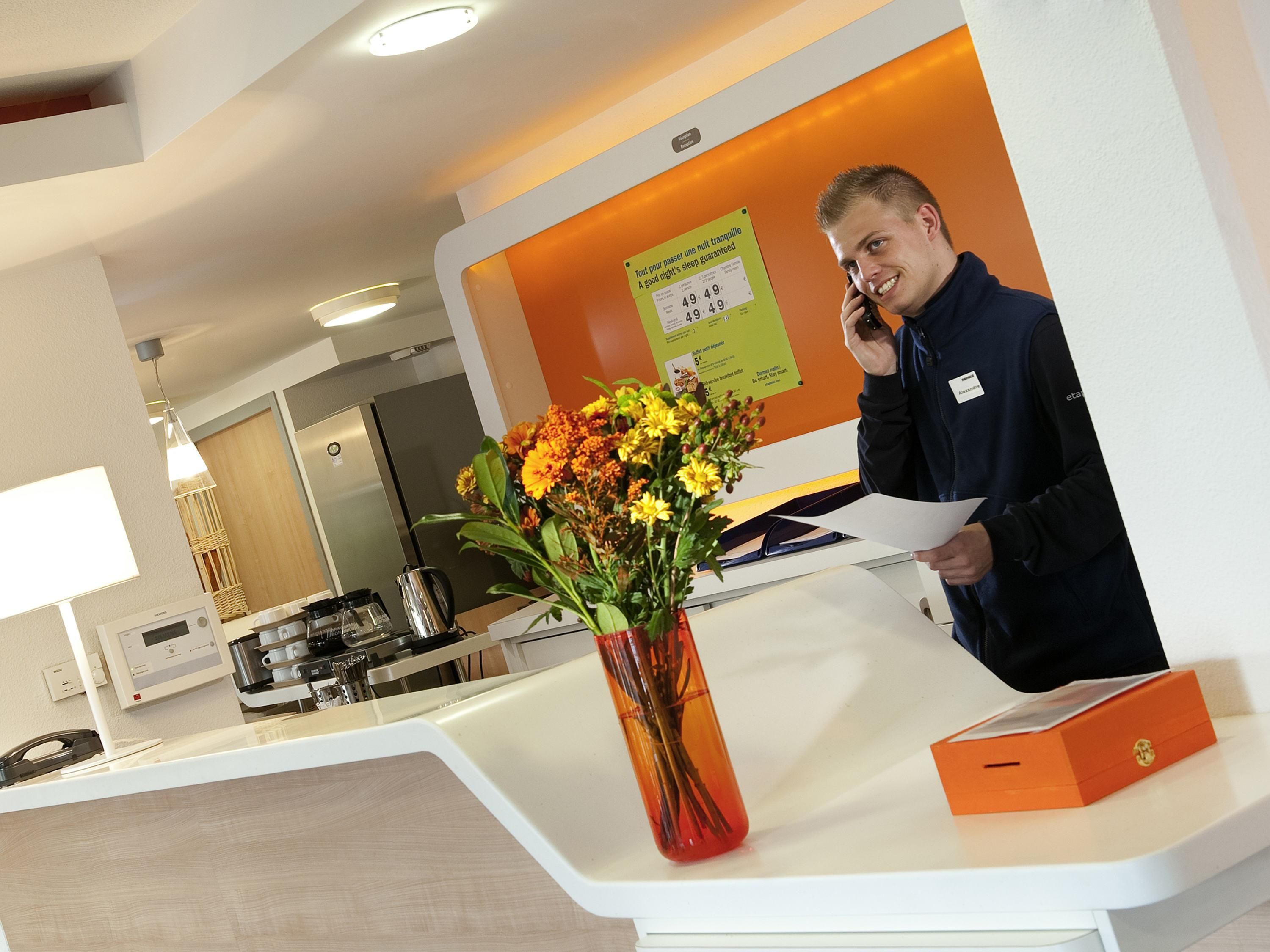 A hotel reception desk with a vase of flowers, a name tag, and a sign about room rates.