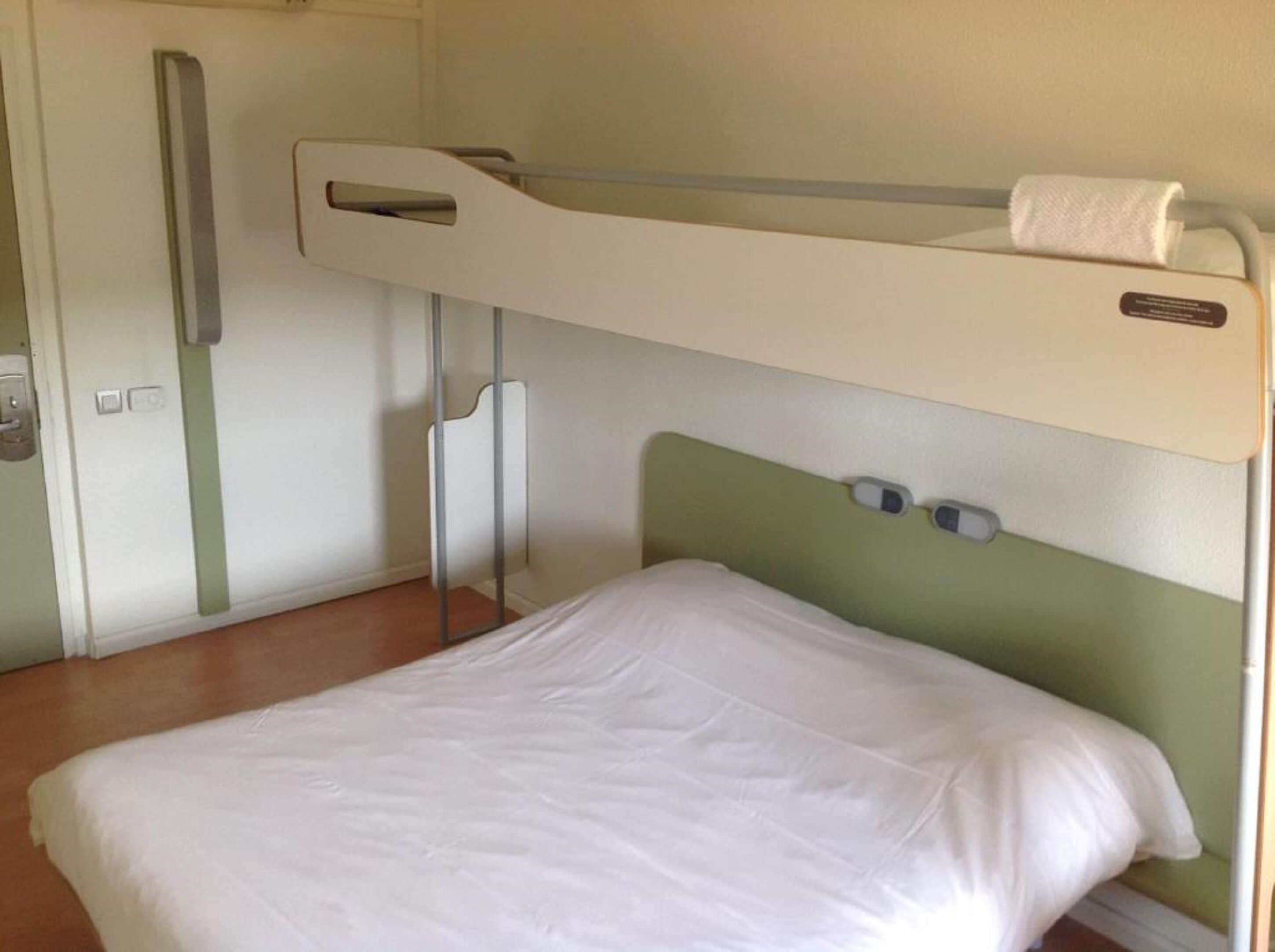 A bunk bed with a green headboard, a white mattress, and a small window.