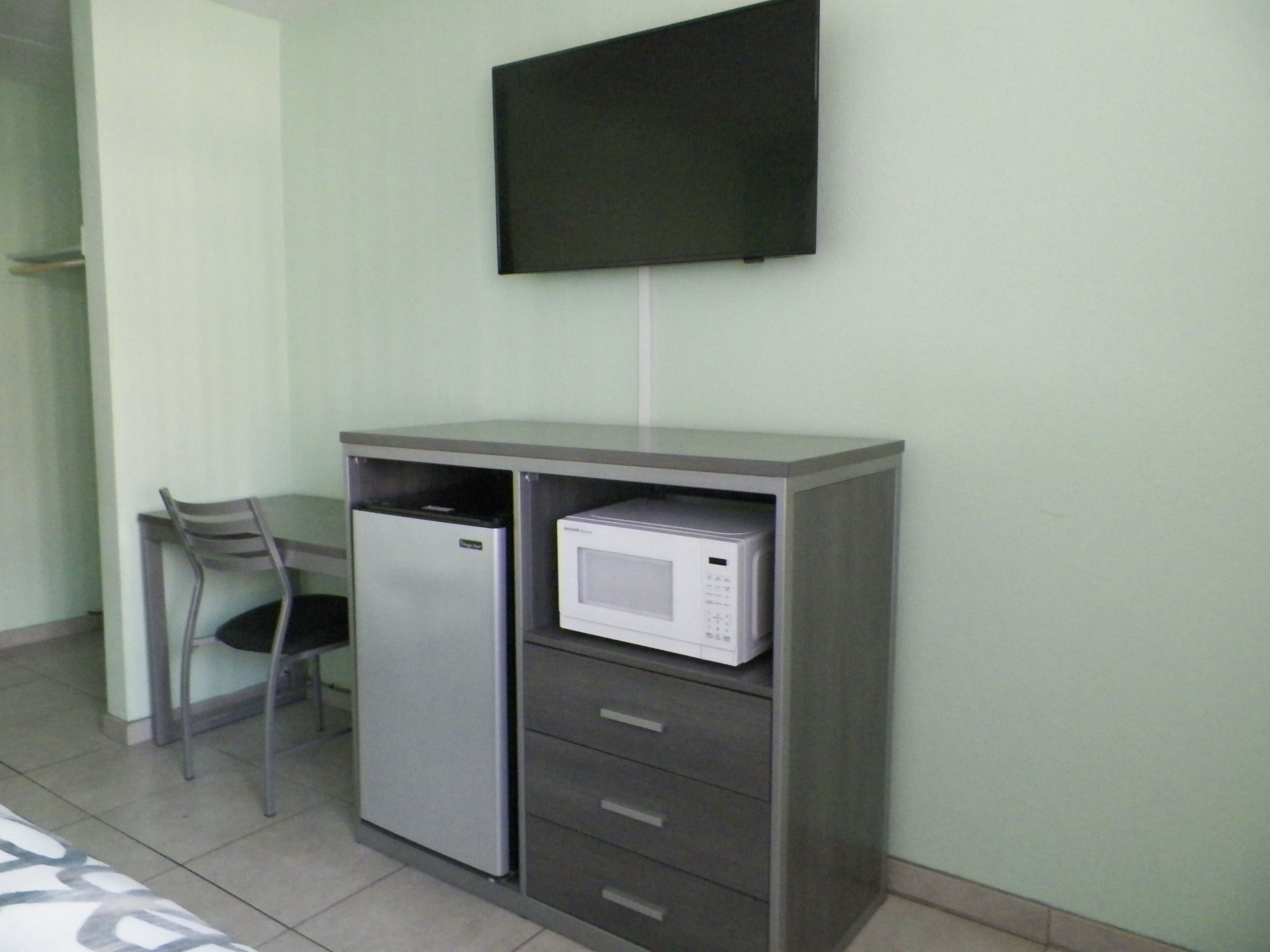A kitchenette with a refrigerator, microwave, and a chair.