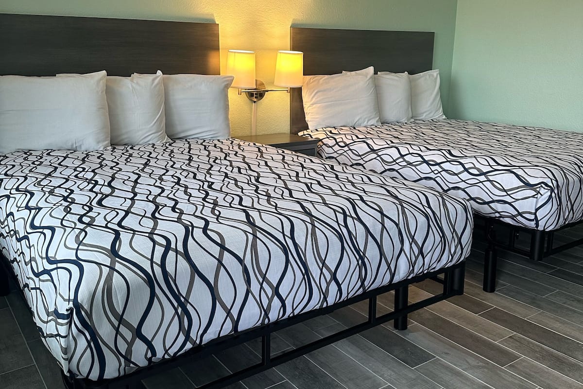 A hotel room with two beds, a headboard, wall-mounted lamps, and a tiled floor.