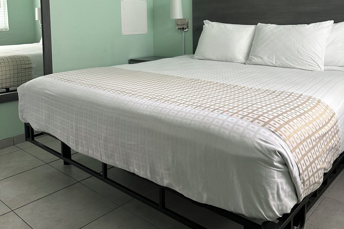 A neatly made bed with a patterned bedspread, a dark headboard, and a framed picture above it.
