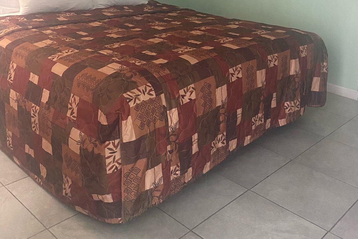 A bed with a patterned quilt, a headboard, and a framed picture on the wall.