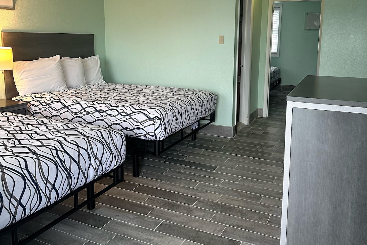 A hotel room with two beds, a desk, and a bathroom visible through an open door.