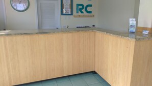 A reception area with a wooden counter, a clock, and a sign for the Royal Canadian Motel. - Royal Canadian Motel (Wildwood)