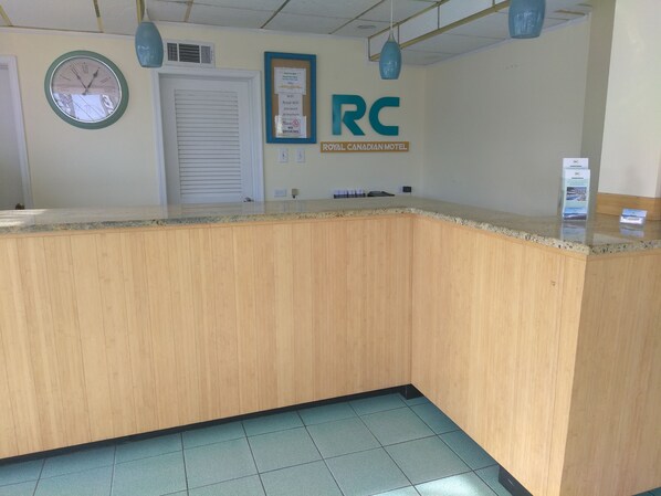 A reception area with a wooden counter, a clock, and a sign for the Royal Canadian Motel. - Royal Canadian Motel (Wildwood)