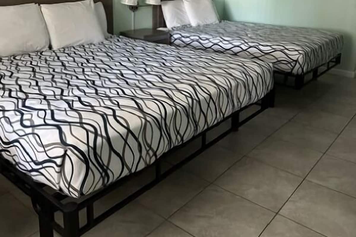 A hotel room with two beds, each with a patterned bedspread, a nightstand with lamps, and light green walls.