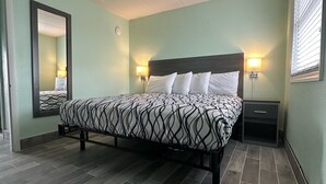 A neatly arranged bedroom with a bed, bedside lamps, a nightstand, and a mirror. - Royal Canadian Motel (Wildwood)