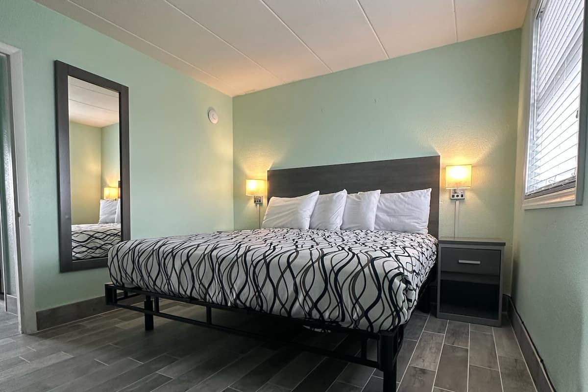 A neatly arranged bedroom with a bed, bedside lamps, a nightstand, and a mirror.
