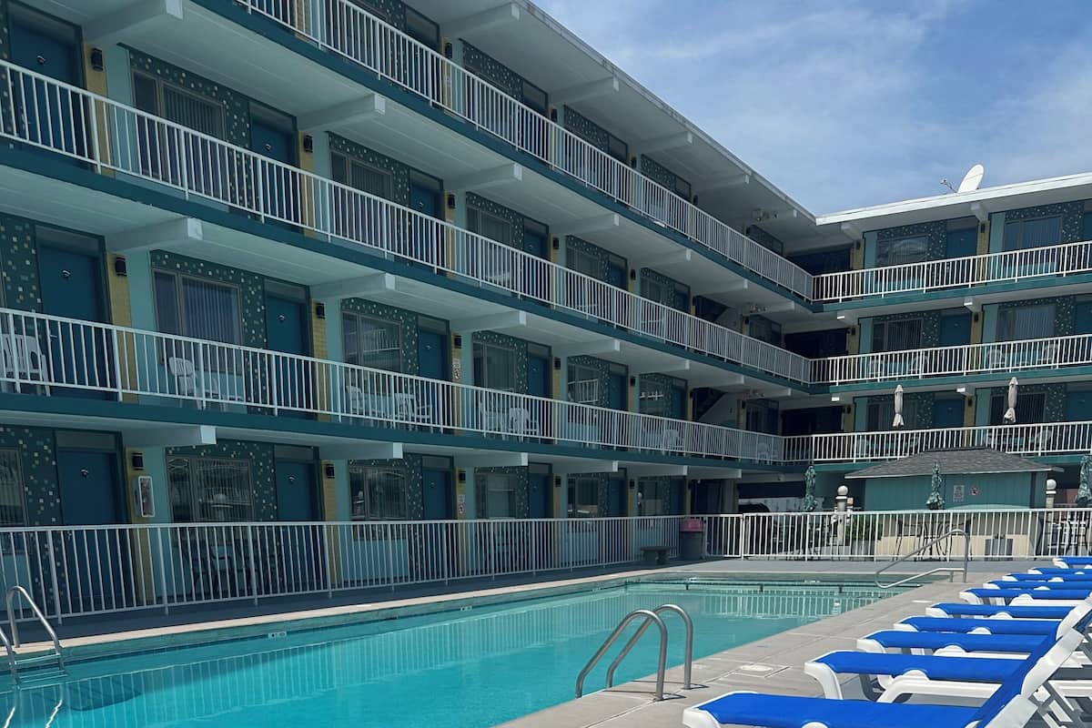 A pool area with lounge chairs and a multi-story building with balconies.