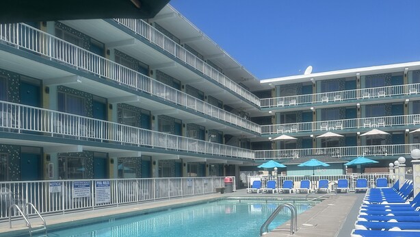 A pool area with blue lounge chairs, a swimming pool, and a multi-story building with balconies. - Royal Canadian Motel (Wildwood)